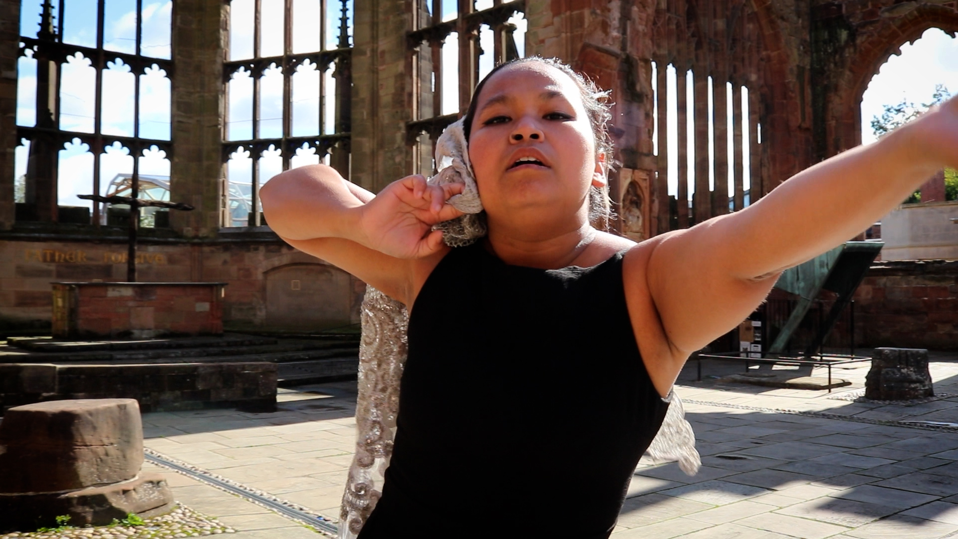 Image of woman dancing with one arm up. Coventry Cathedral is in the background