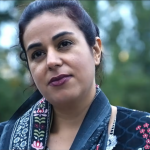 Still from film of Navkiran Mann reading poem. She is outside there are trees in the background